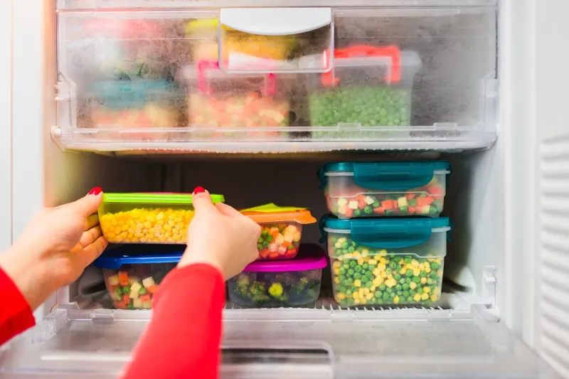 woman placing container with frozen mixed vegetables in refrigerator