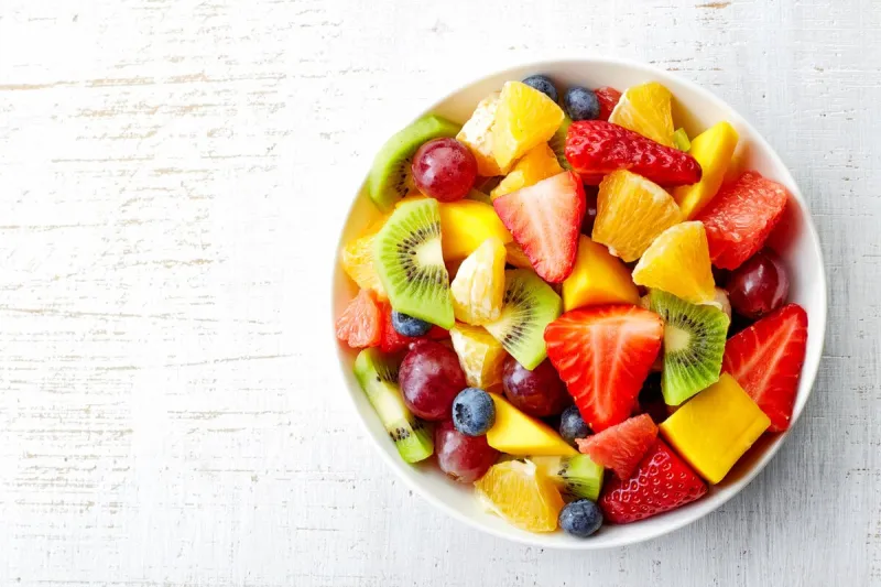 bowl of healthy fresh fruit salad on wooden background top view