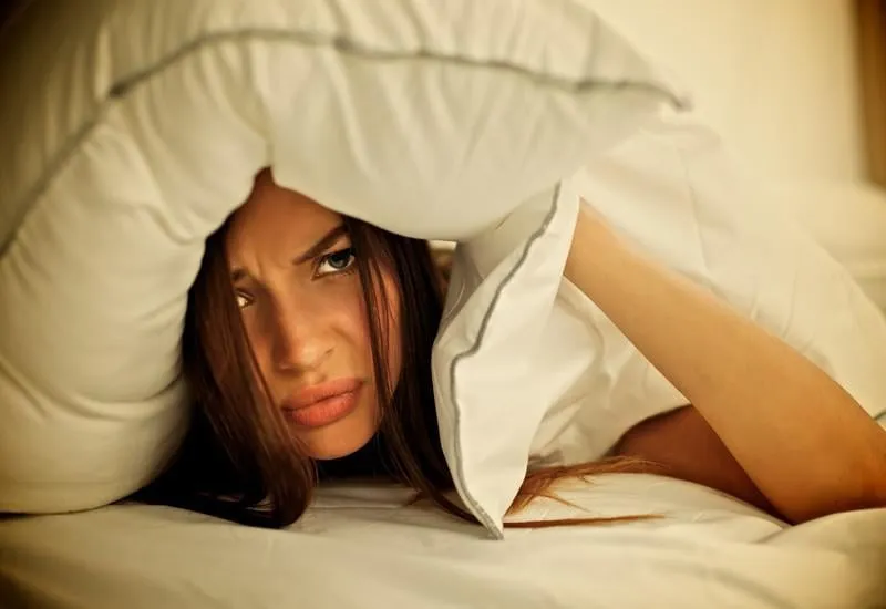 femme couchée sur le lit et en fermant les oreilles avec oreiller