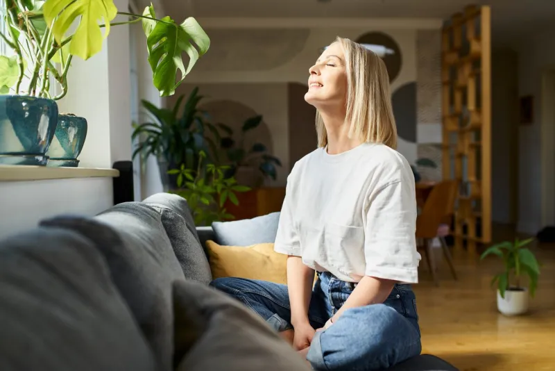 happy adult woman sitting on the sofa with eyes closed enjoying bright daylight