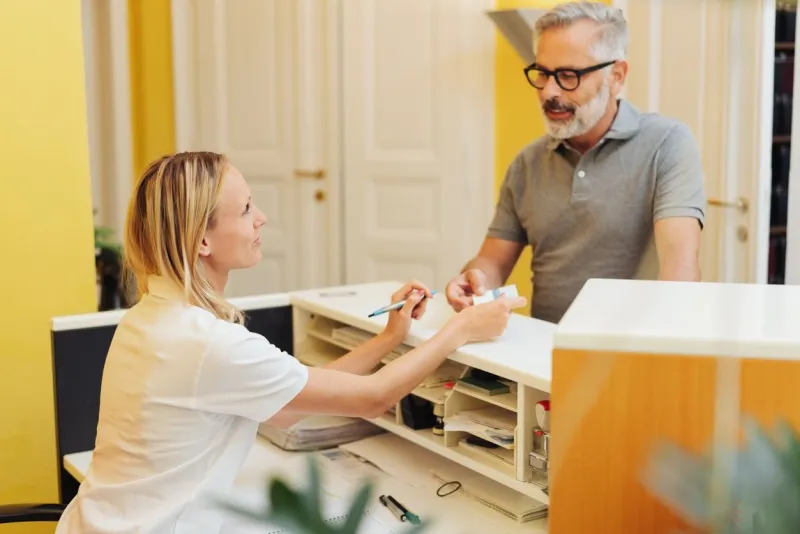 patient settling up with a receptionist in a medical surgery after an examination by a doctor or dentist