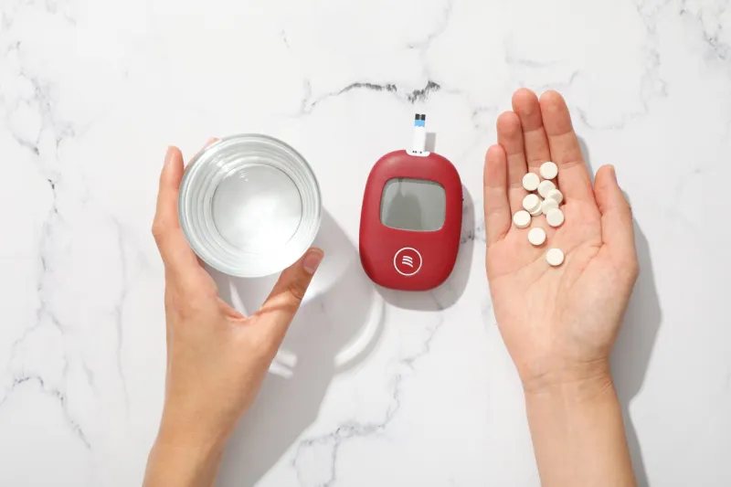 medical equipment for diabetics, pills and glass of water in female hands on marble background, top view