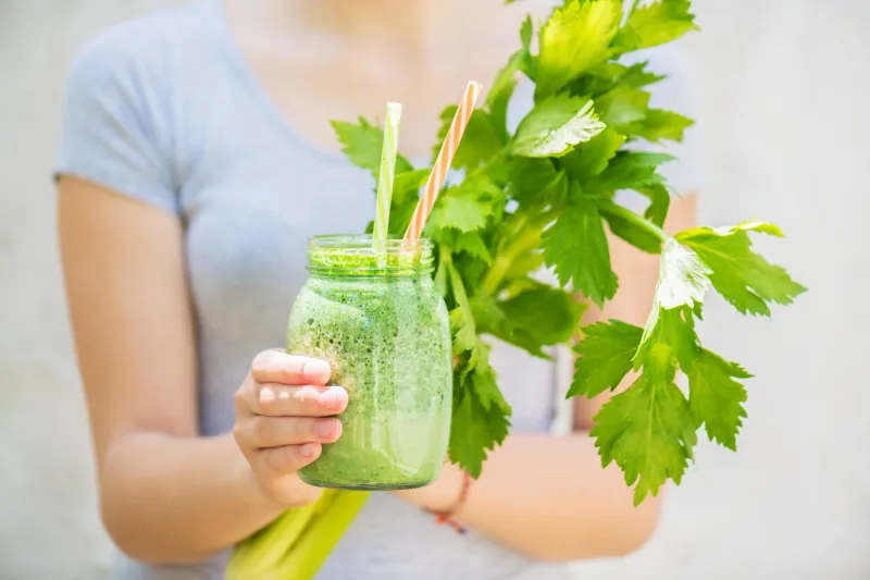 a young girl holds a jar of green smoothie and fresh celery in her hands summer vitamin and nutritious drink for the whole family detox and healthy eating concept