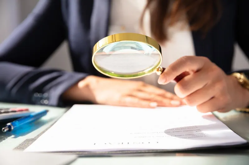 close-up of a businesswoman's hand looking at contract form through magnifying glass