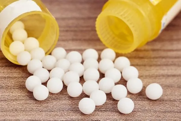 granules homéopathiques dispersés sur une table en bois près de leurs récipients jaunes