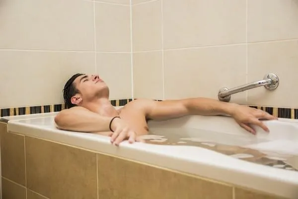 beau jeune homme dans la baignoire à la maison ayant un bain, laver le corps et les cheveux avec bathfoam et shampooing