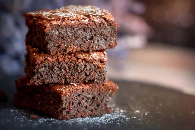 homemade dark chocolate fudge brownies cake stacked on stone plate with copy space lavender flowers background