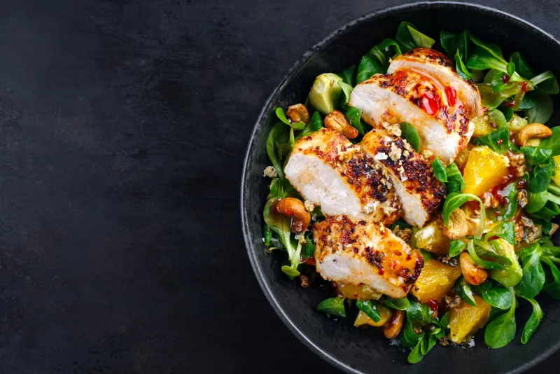 traditional german lamb’s lettuce with chicken breast, fruit and cashew nuts served with spicy sweet and sour sauce as top view on a nordic design bowl with copy space left