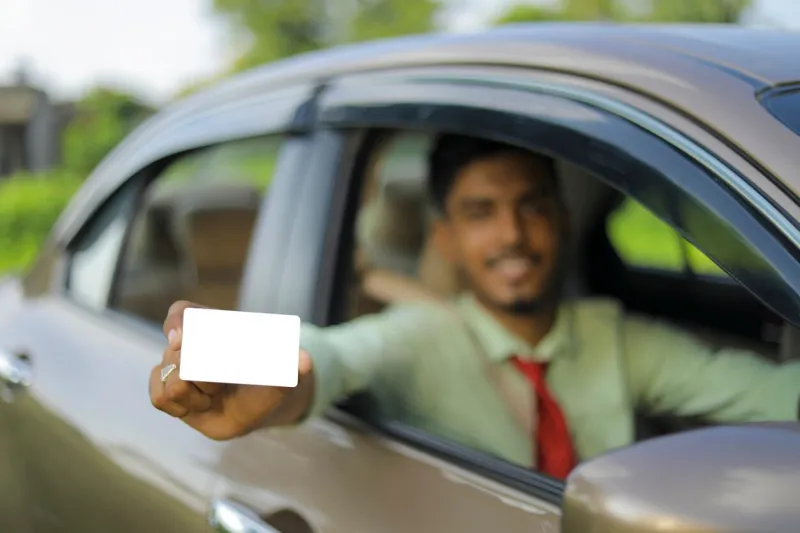 young indian businessman or employee sitting in car and showing card