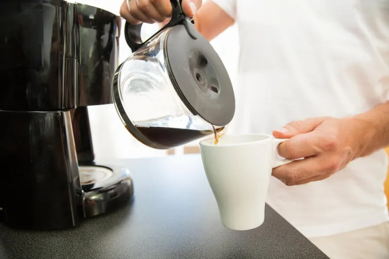 homme dans la cuisine verser une tasse de café chaud filtré à partir d'un pot de verre en prenant le petit déjeuner le matin