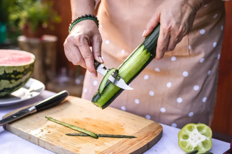 woman peeling cucumber making fresh vegetable salad outdoors preparing raw food