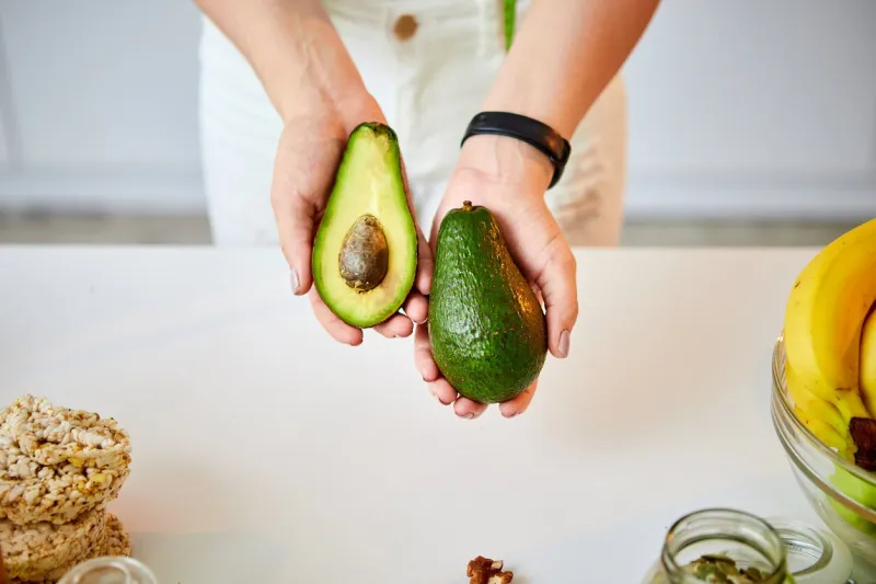 young happy woman holding avocado for making salad in the beautiful kitchen with green fresh ingredients indoors healthy food and dieting concept loosing weight