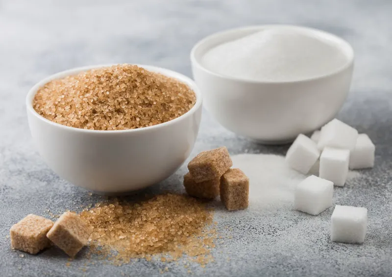 white bowl plates of natural brown and white refined sugar and cubes on light background