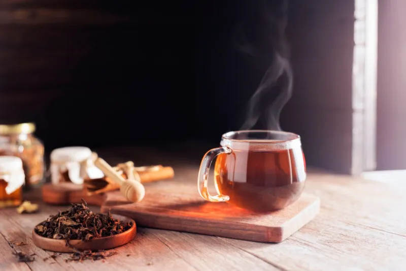 cup or tea glass hot brew and dried tea leaves on a wooden plate, placed on a wooden table, on a dark black background