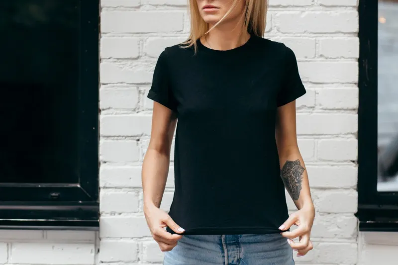 stylish blonde girl wearing black t-shirt and glasses posing against street , urban clothing style