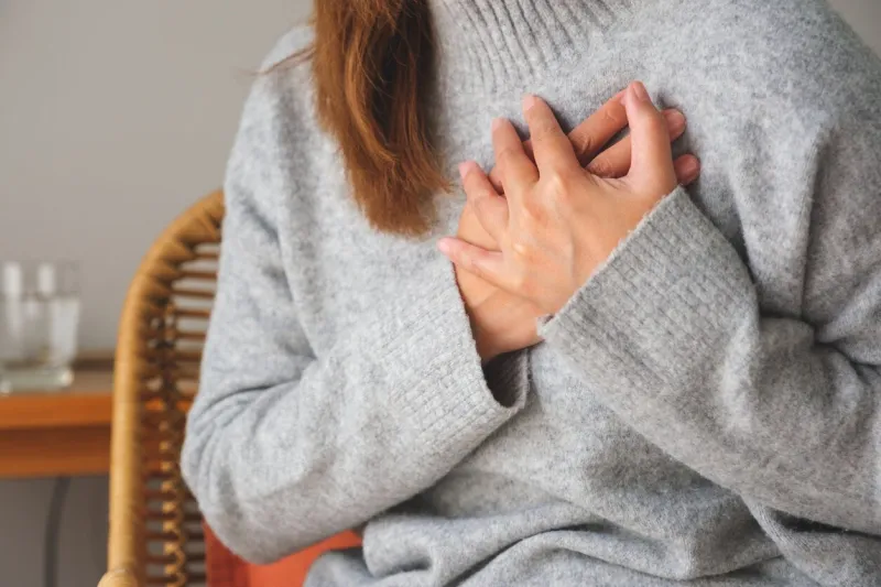 closeup image of a woman with hands on chest, sudden heart attack, suffering from chest pain