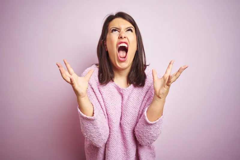 young beautiful brunette woman wearing a sweater over pink isolated background crazy and mad shouting and yelling with aggressive expression and arms raised frustration concept