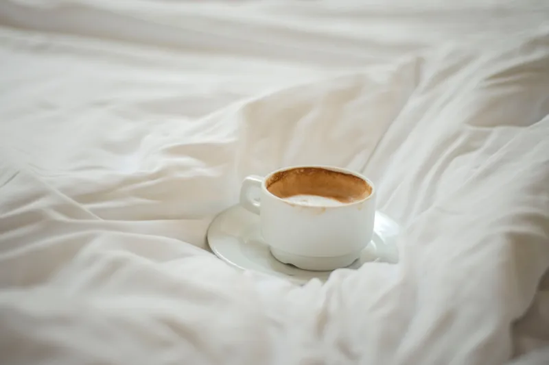 a cup of coffee on a rumpled bed, morning coffee in bed