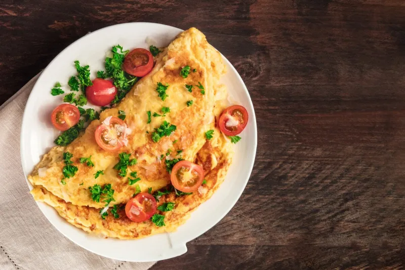 a photo of an omelet with cherry tomatoes, parsley and grated cheese, shot from above on a rustic wooden texture with a place for text