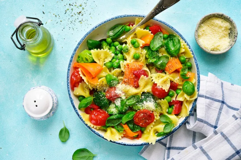 pasta primavera with spring vegetables in a white vintage bowl on a light blue slate, stone or concrete backgroundtop view