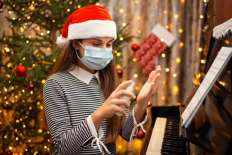 cheerful girl in red santa hat and protective medical mask applying hand sanitizer to hands while playing the piano
