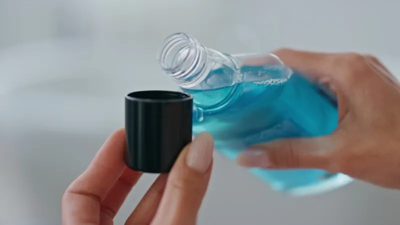 woman hands pouring mouthwash in cap indoors close up unknown lady holding blue antibacterial liquid at bathroom unrecognizable girl using refreshing dental rinse morning care in bath room concept