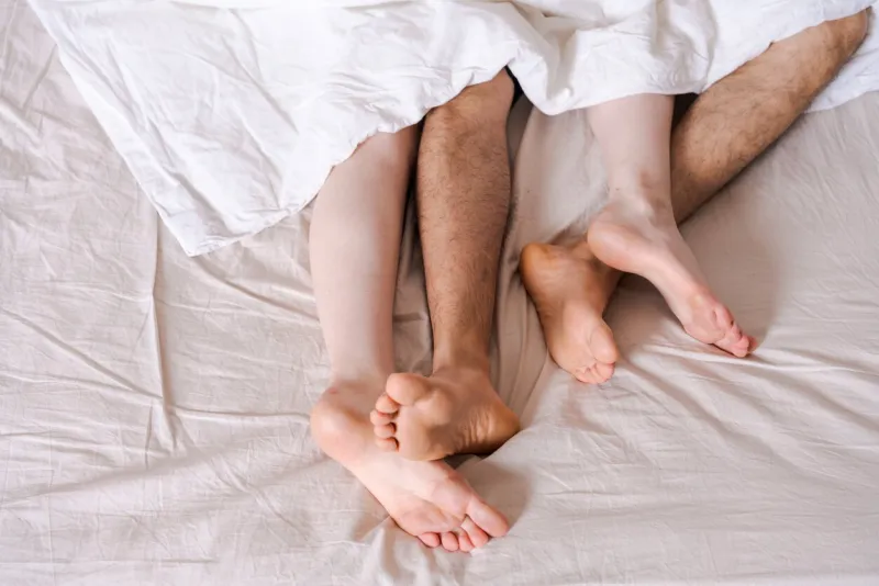 feet of a couple in bed under the white blanket