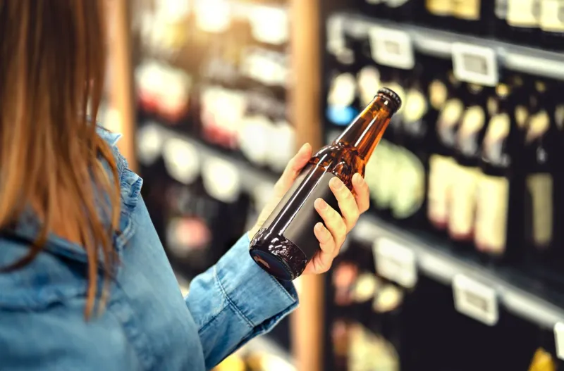 customer buying beer in liquor store lager, craft or wheat beer ipa or pale ale woman at alcohol shelf drink section and aisle in supermarket lady holding bottle in hand drink business concept