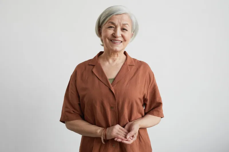 minimal waist up portrait of modern senior woman smiling at camera while standing against white background