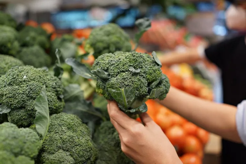 woman's hand choosing fresh broccoli in supermarket concept of healthy vegetarian food