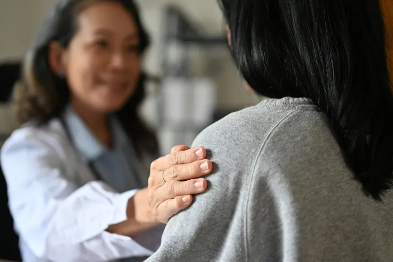 an aged asian female doctor touching shoulder to comfort and support her patient a young asian female patient is being reassured by her doctor close-up image