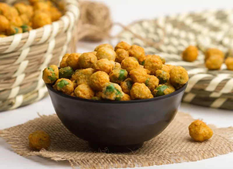 fried green peas with chili served in a bowl isolated on napkin side view of nuts on grey background
