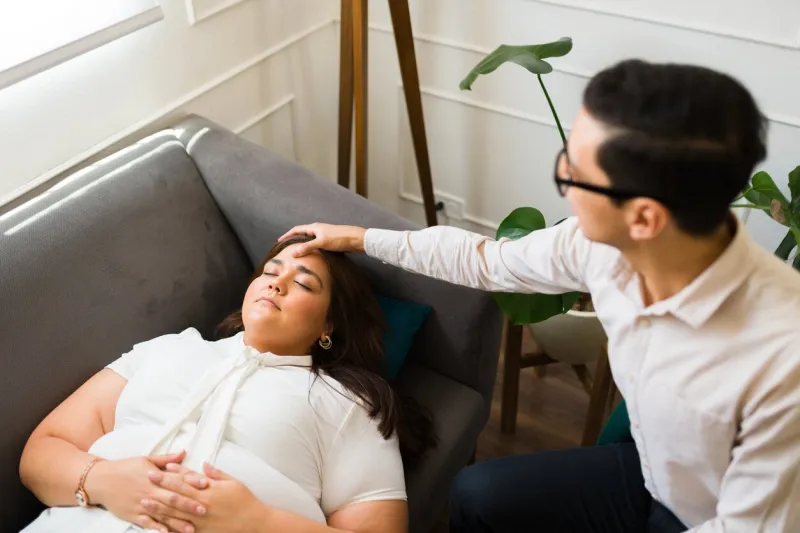 psychologist touching the forehead of a patient lying on the couch and trying hypnosis therapy to help with mental health problems