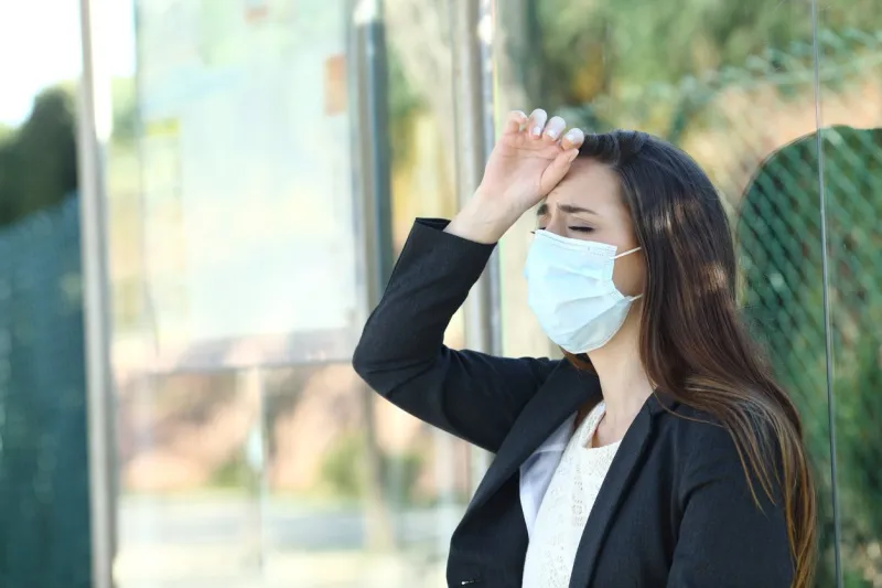 woman wearing a protective mask complaining suffering head ache in a bus stop