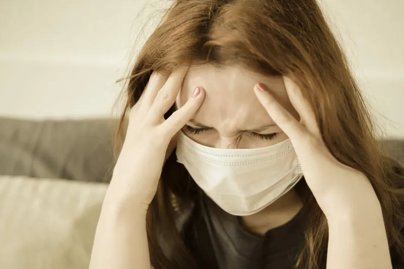 a redhead girl in a medical mask has a headache woman with a sore head sits on the bed