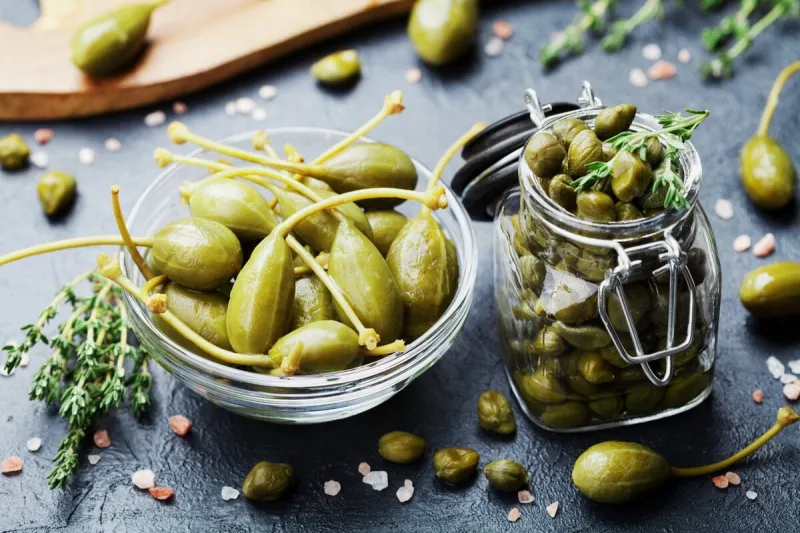 mixed capers in jar and bowl on black stone kitchen table