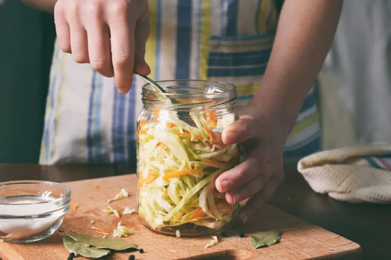 woman cook sauerkraut or salad on wooden background step 5 - put the cabbage in the jars fermented preserved vegetables food concept