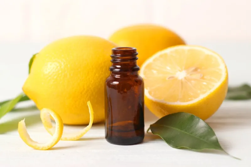 bottle of essential oil of lemon and lemons on a light backgroun