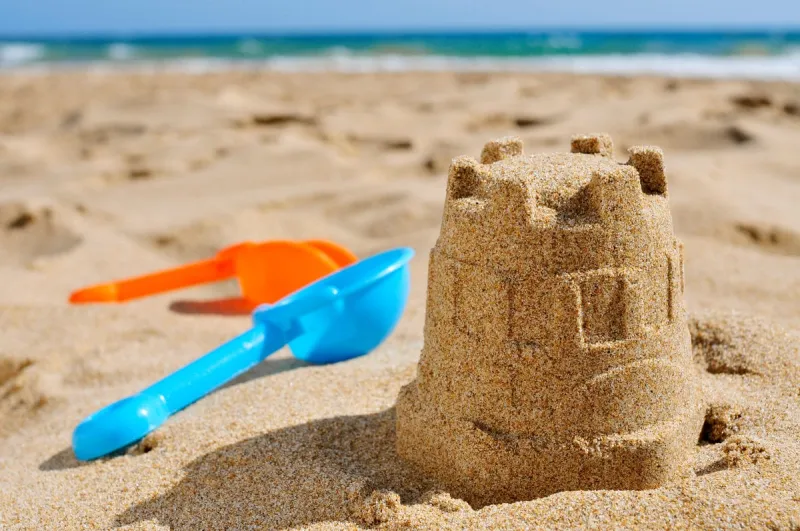 closeup of a sandcastle and toy shovels of different colors on the sand of a beach