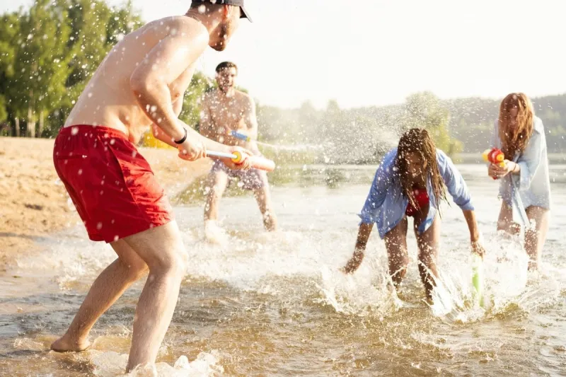 happy friends doing battle with water guns - youth, summer lifestyle and holiday concept