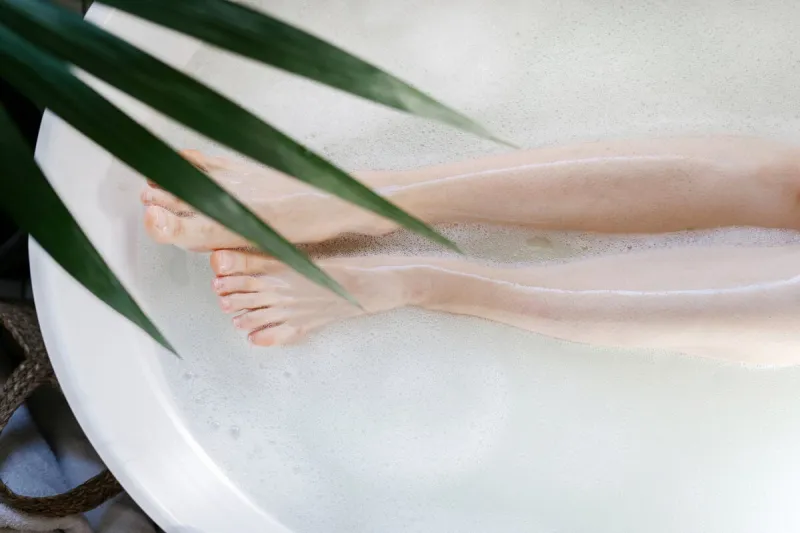 cropped shot of female legs top view of woman lying in bathroom tub with warm water and bubbles epilation, depilation, skin care concept girl take bath in tropical hotel, enjoy beauty spa procedure