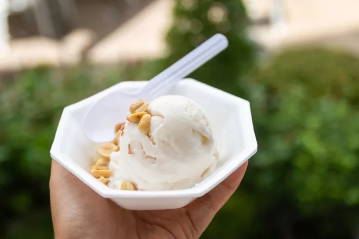hand holding take away cup of coconut ice cream with nature green garden background happy walking and eating in hot weather