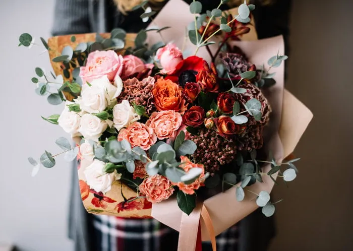 very nice young woman holding big beautiful blossoming ombre bouquet of fresh roses, carnations and eucalyptus flowers in gradient colors from white to vivid red on the grey wall background