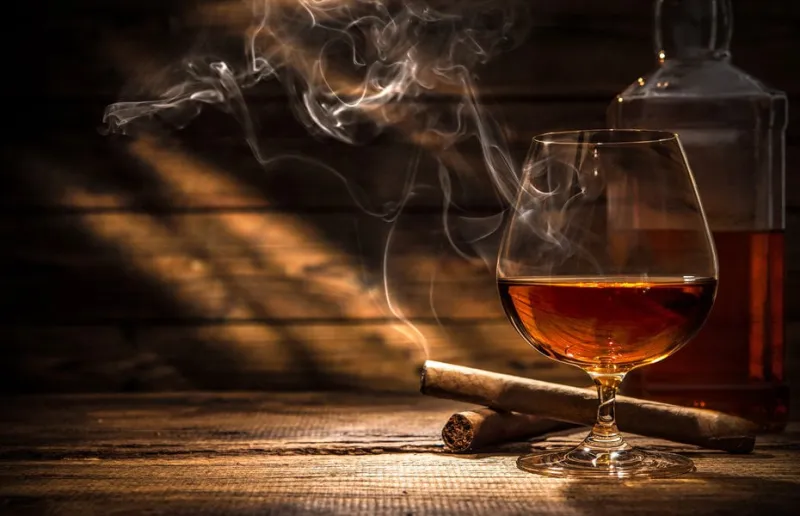 glass of whiskey with smoking cigar and ice cubes on wooden table
