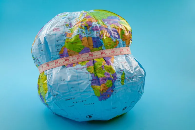 global obesity epidemic crisis affecting increasing numbers of earth population and chronic health condition concept with globe and measuring tape isolated on blue background