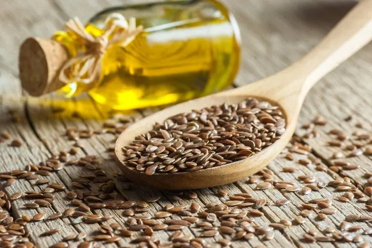heap of flax seeds or linseeds in spoon and bowl with glass of linseed oil on wooden backdrop flaxseed or linseed concept flax seed dietary fiber