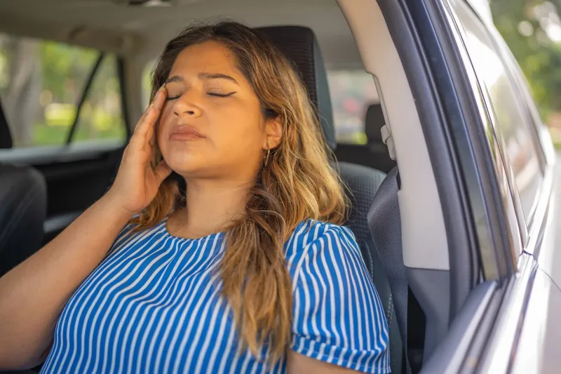 woman with migraine sitting in car, with hand on head