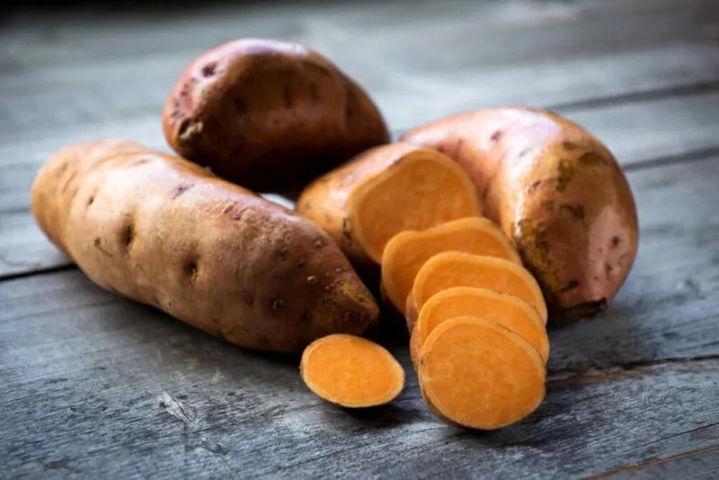 raw sweet potatoes on wooden background closeup