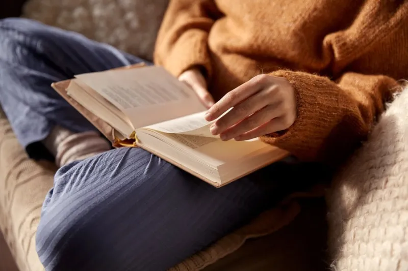 people, season and leisure concept - close up of woman in warm sweater reading book at home