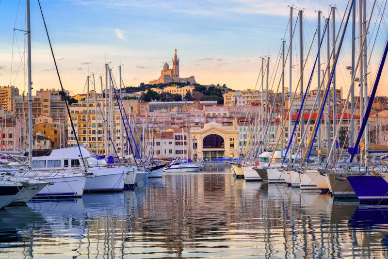 yachts reflecting in the still water of the old vieux port of marseilles beneath cathedral of notre dame, france, on sunrise